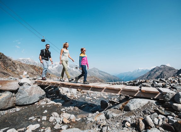 Family hiking across the bridge along the glacier path, the gondola in the background
